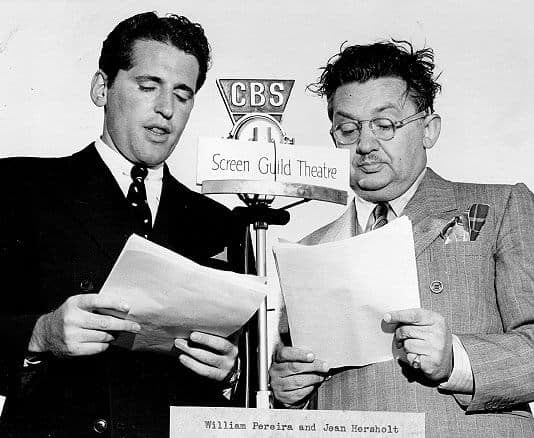 Two men in suits stand next to a microphone labeled "CBS" and "Screen Guild Theatre," reading from scripts. A sign in front of the microphone names "William Pereira and Jean Hersholt.