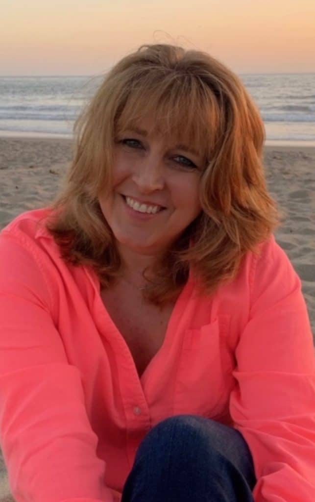 A woman in a pink shirt sitting on the beach.