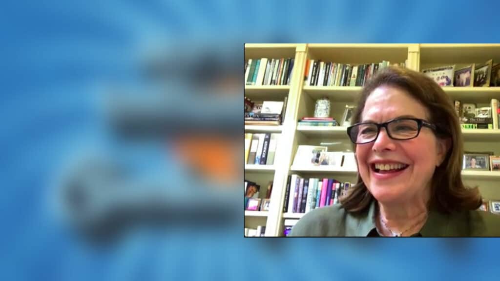 A woman in glasses is smiling in front of a book shelf.