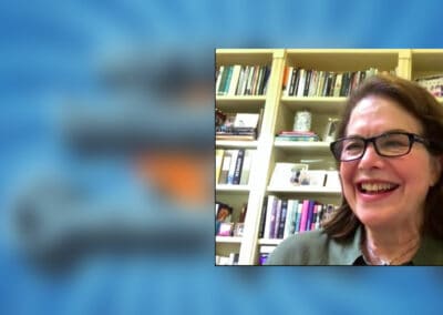 A woman in glasses is smiling in front of a book shelf.