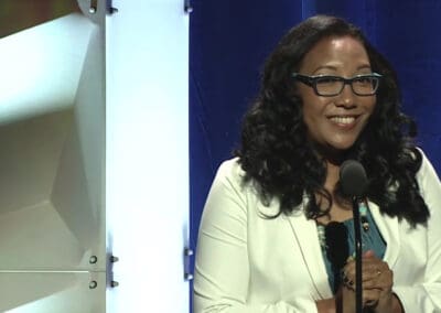 A woman in glasses is standing in front of a microphone.