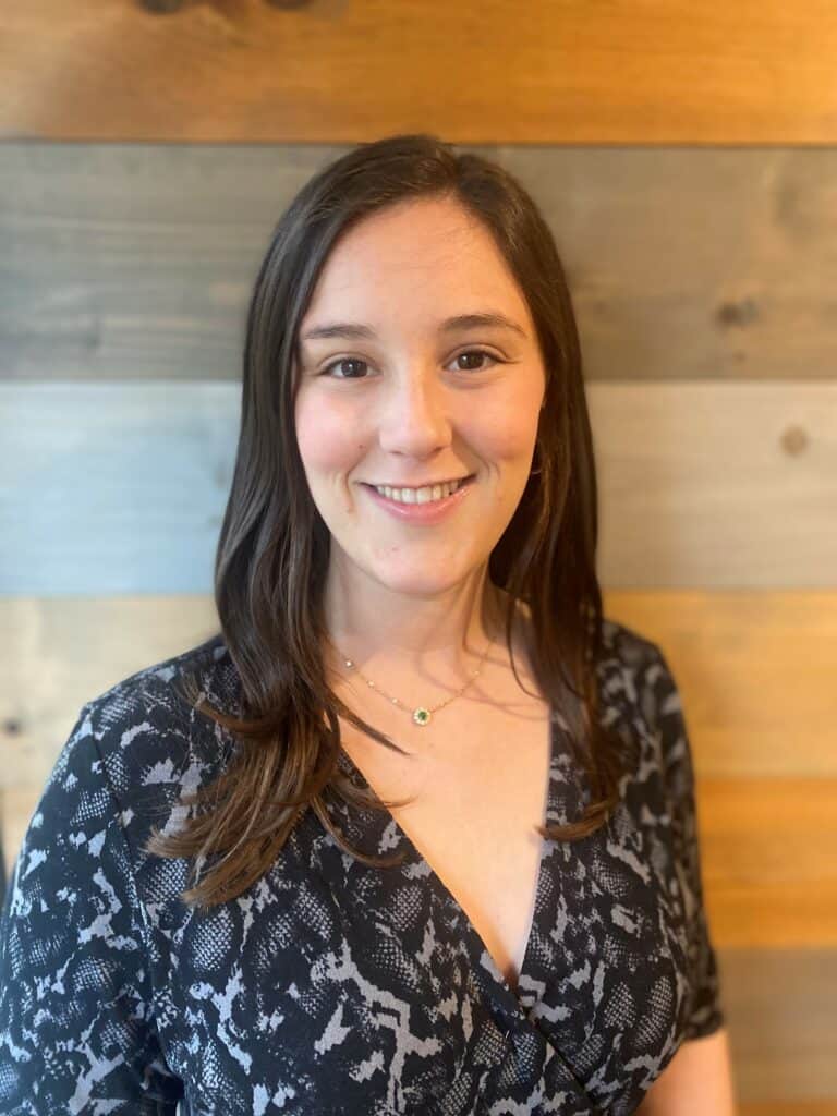 A woman smiling in front of a wooden wall.