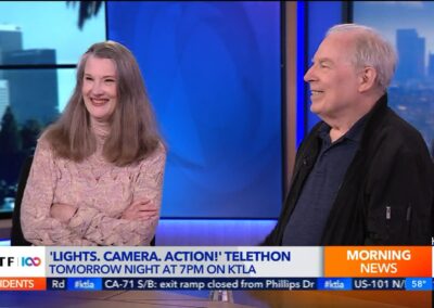 A man and woman are sitting on a television set.