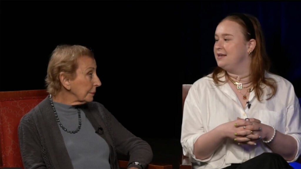 Two women sitting in a chair talking to each other.