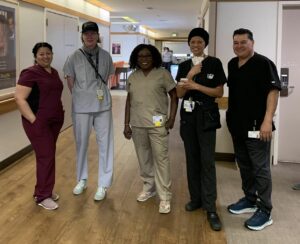 Five healthcare professionals in scrubs stand in a hallway under an exit sign, posing for a group photo.