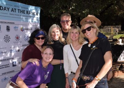 A group of people smiling at a daytime outdoor event, standing in front of a sign with sponsors' logos.